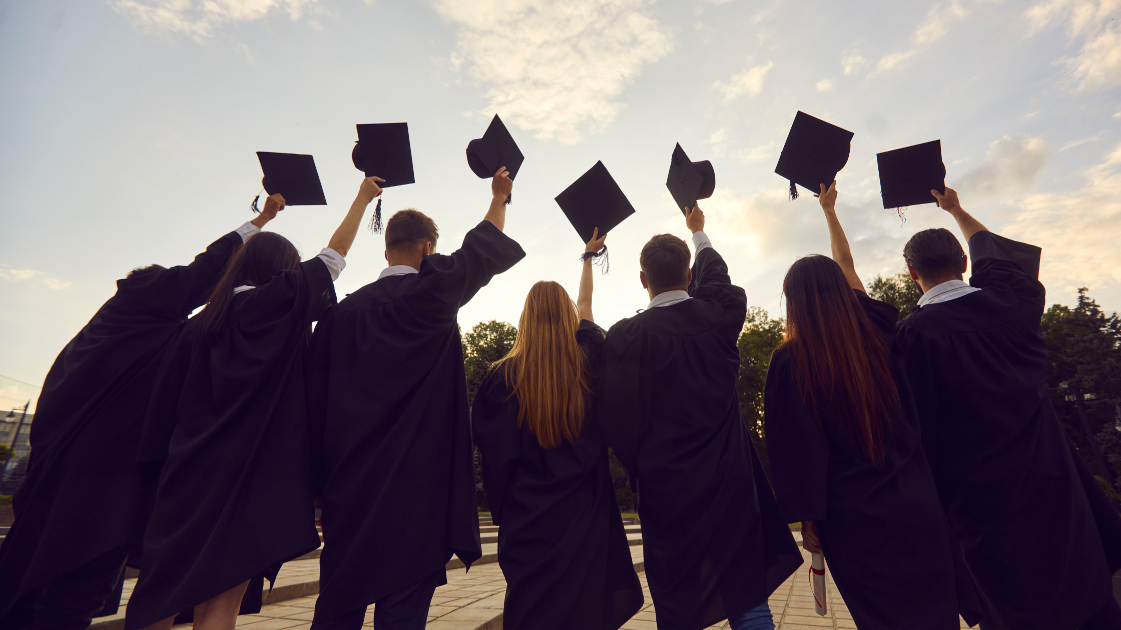 PhdAdmissionsGuidebyGlobalAdmissions Graduates in gowns raising their caps to the sky.